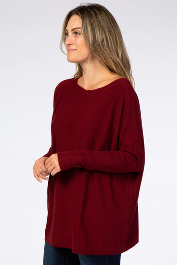 woman wearing a burgundy oversized knit sweater and blue jeans against a white background
