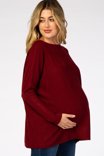 woman wearing a burgundy oversized maternity sweater and holding her baby bump