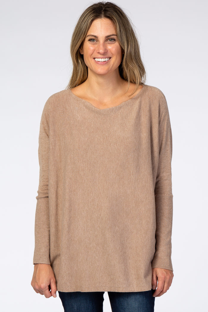 woman wearing a beige oversized sweater with long sleeves and a wide neckline, styled with dark blue jeans