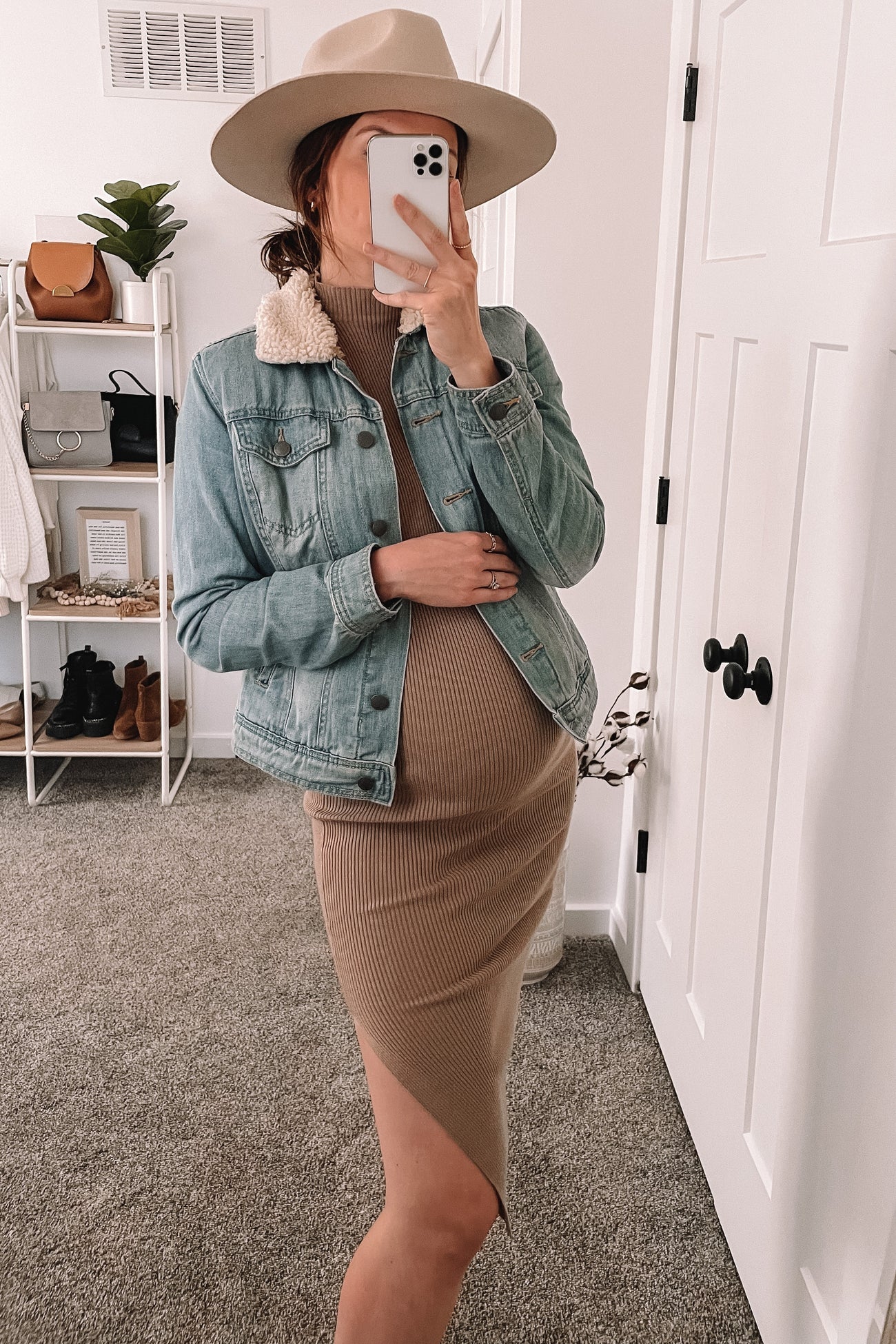 woman wearing a light blue denim maternity jacket over a brown ribbed maternity dress with a visible baby bump