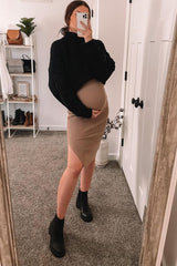 woman wearing a black oversized sweater and a beige form-fitting maternity dress, showing her baby bump