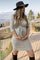 woman wearing a gray maternity wrap dress and holding her baby bump, paired with a wide-brimmed hat and tall boots