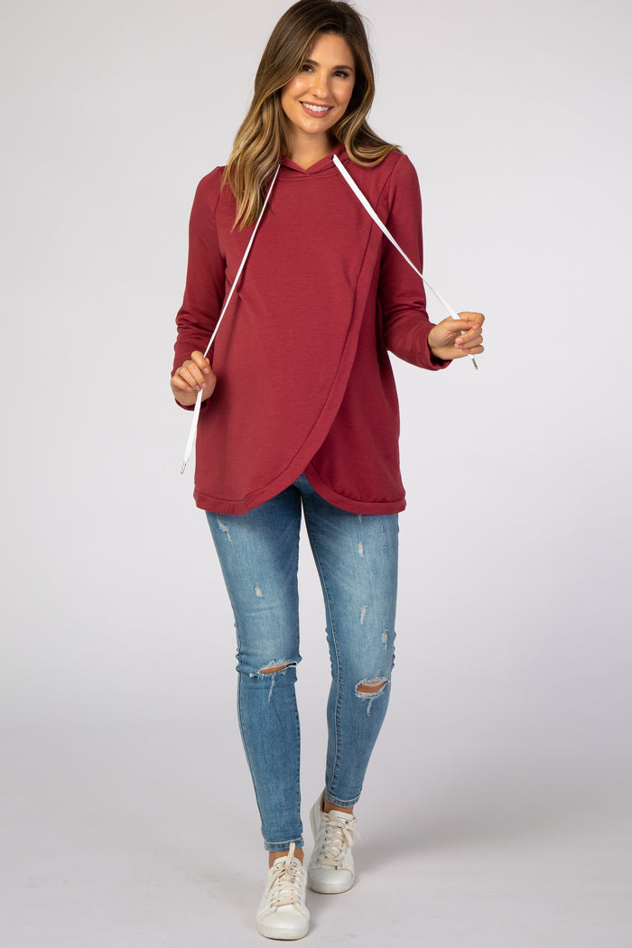 woman wearing a burgundy maternity hoodie with a crossover design and drawstring, paired with distressed skinny jeans