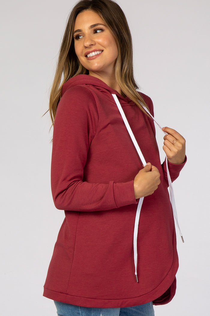 woman wearing a burgundy maternity hoodie with a scalloped hem and a white drawstring, showcasing her baby bump