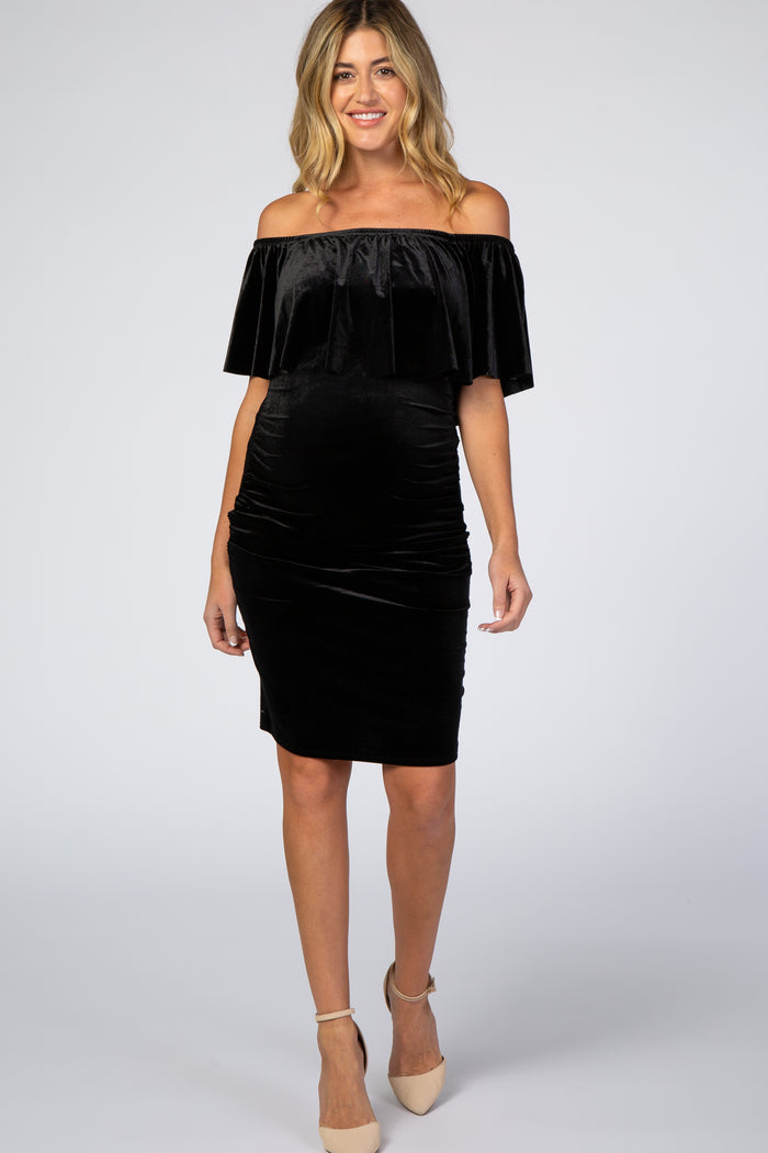 woman wearing a black velvet off the shoulder maternity dress with ruffle detail and beige heels