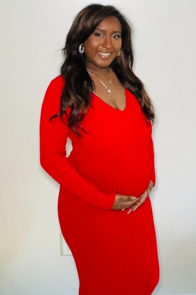 woman wearing a red ribbed maternity dress, showcasing her baby bump with a smile