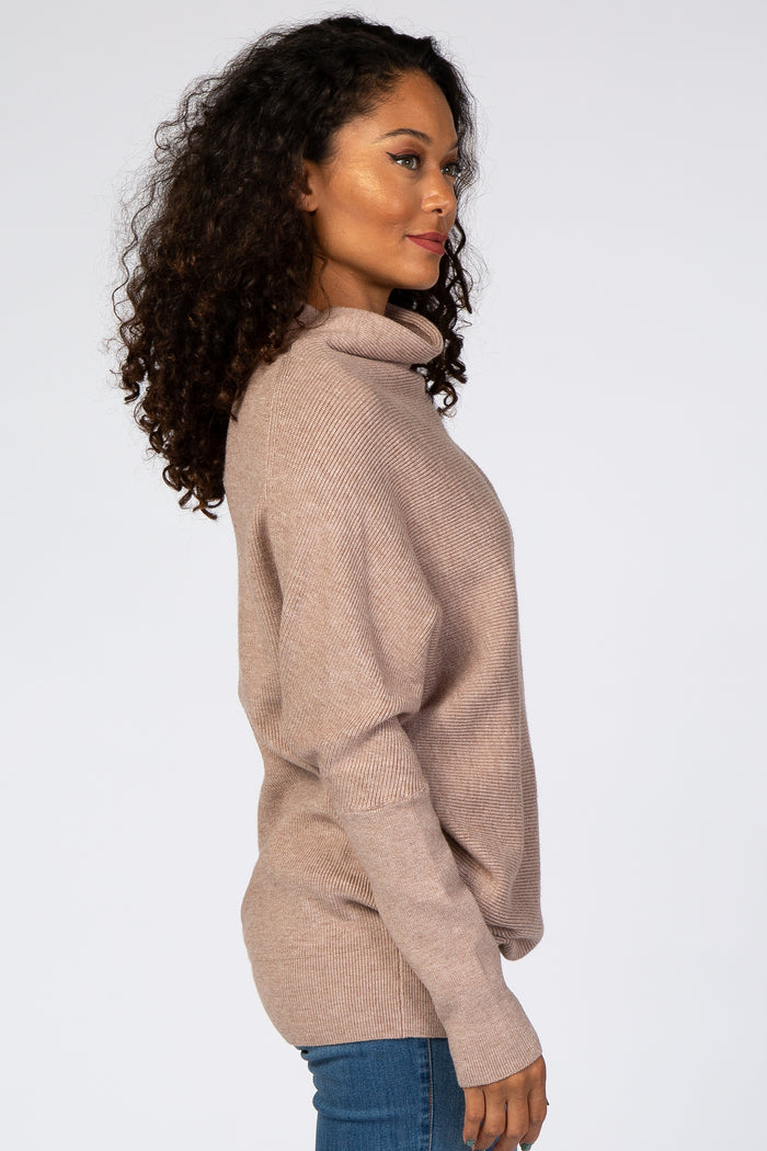 woman wearing a light brown oversized sweater with a cowl neckline and long sleeves, styled with blue jeans
