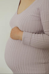 woman wearing a light purple ribbed maternity top, holding her baby bump