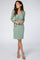 woman wearing a light green wrap dress with three-quarter sleeves and a tie waist, standing on a plain background