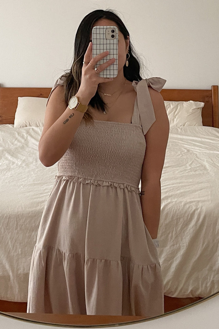 woman wearing a beige smocked midi dress with tie shoulder straps and a tiered skirt, mirror selfie in a bedroom