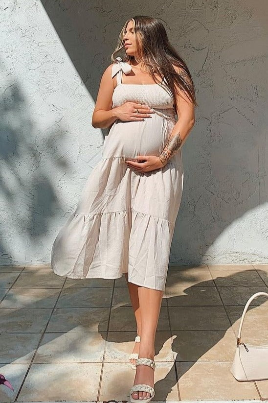 pregnant woman in a beige smocked maternity dress holding her baby bump outdoors