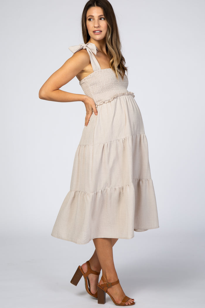 pregnant woman in beige smocked maternity midi dress with tie straps and tiered skirt