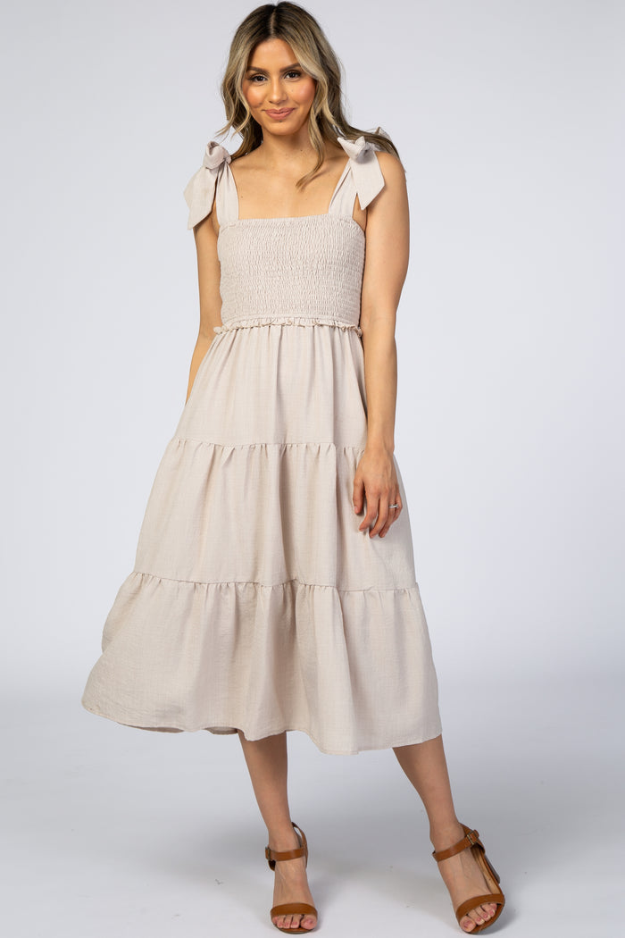 woman wearing a light beige smocked midi dress with tie shoulder straps and a tiered skirt