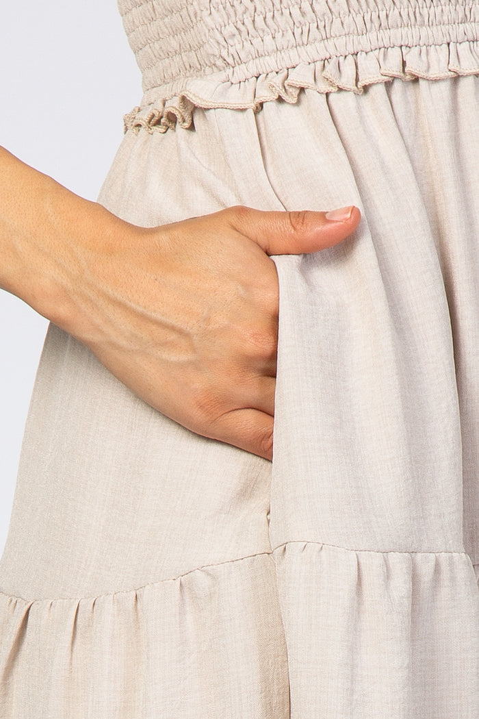 close-up of a woman's hand in the pocket of a light beige smocked dress with ruffle details