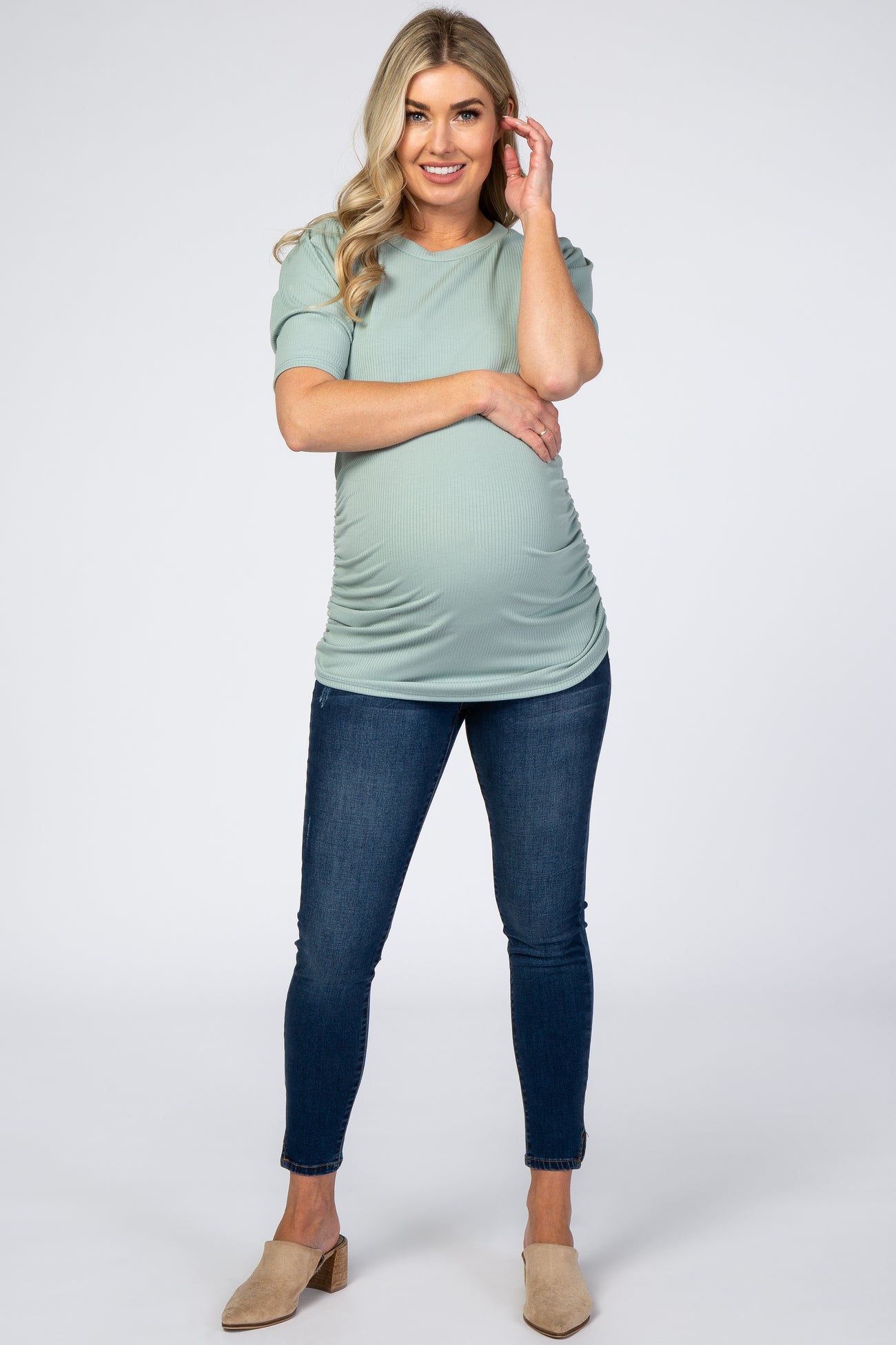 woman wearing a mint green short sleeve maternity top and dark blue skinny jeans, showing her baby bump