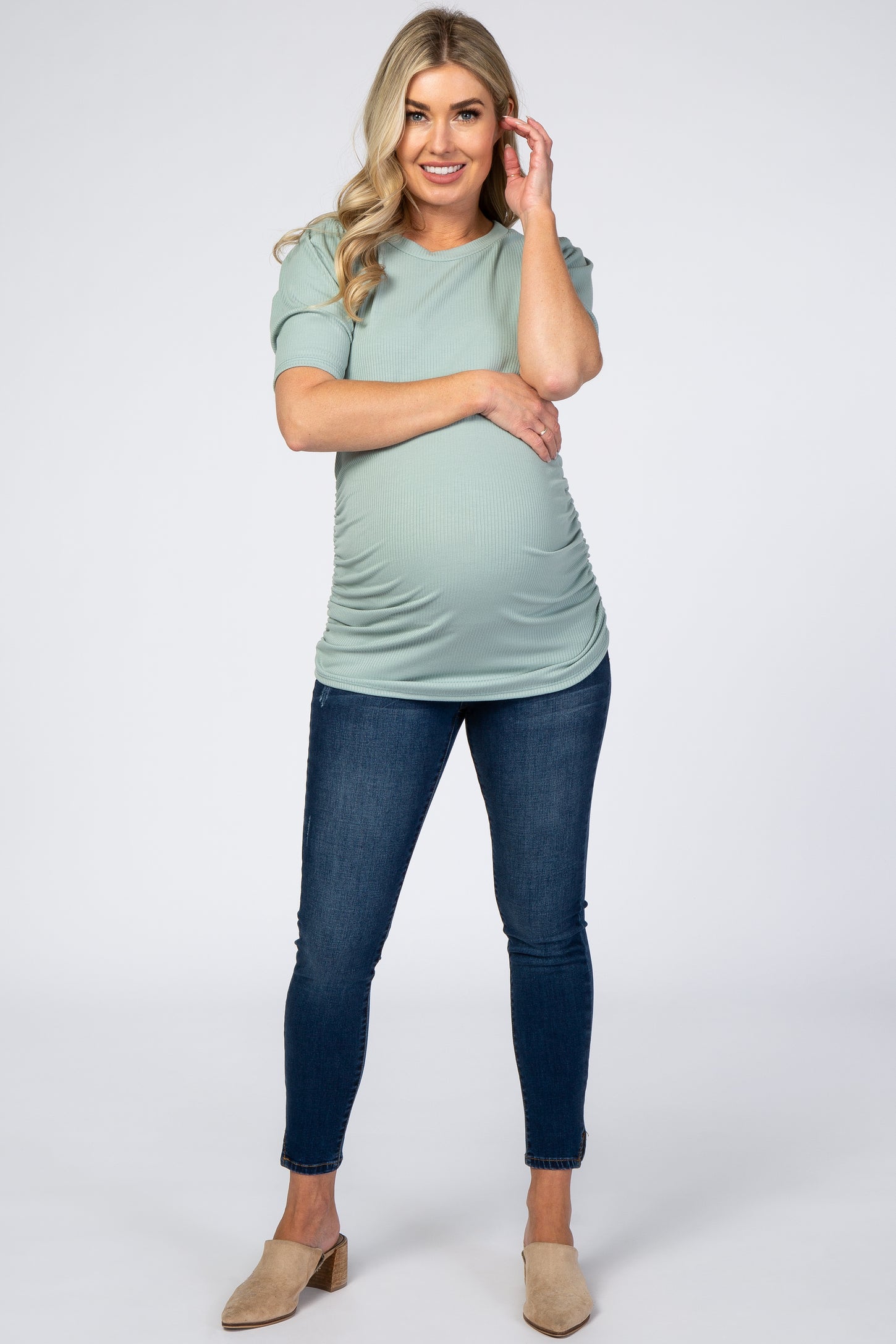 woman wearing a mint green short sleeve maternity top and dark blue skinny jeans, showing her baby bump