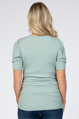 Back view of a woman wearing a sage green ribbed short sleeve maternity top with puffed shoulders and side ruching