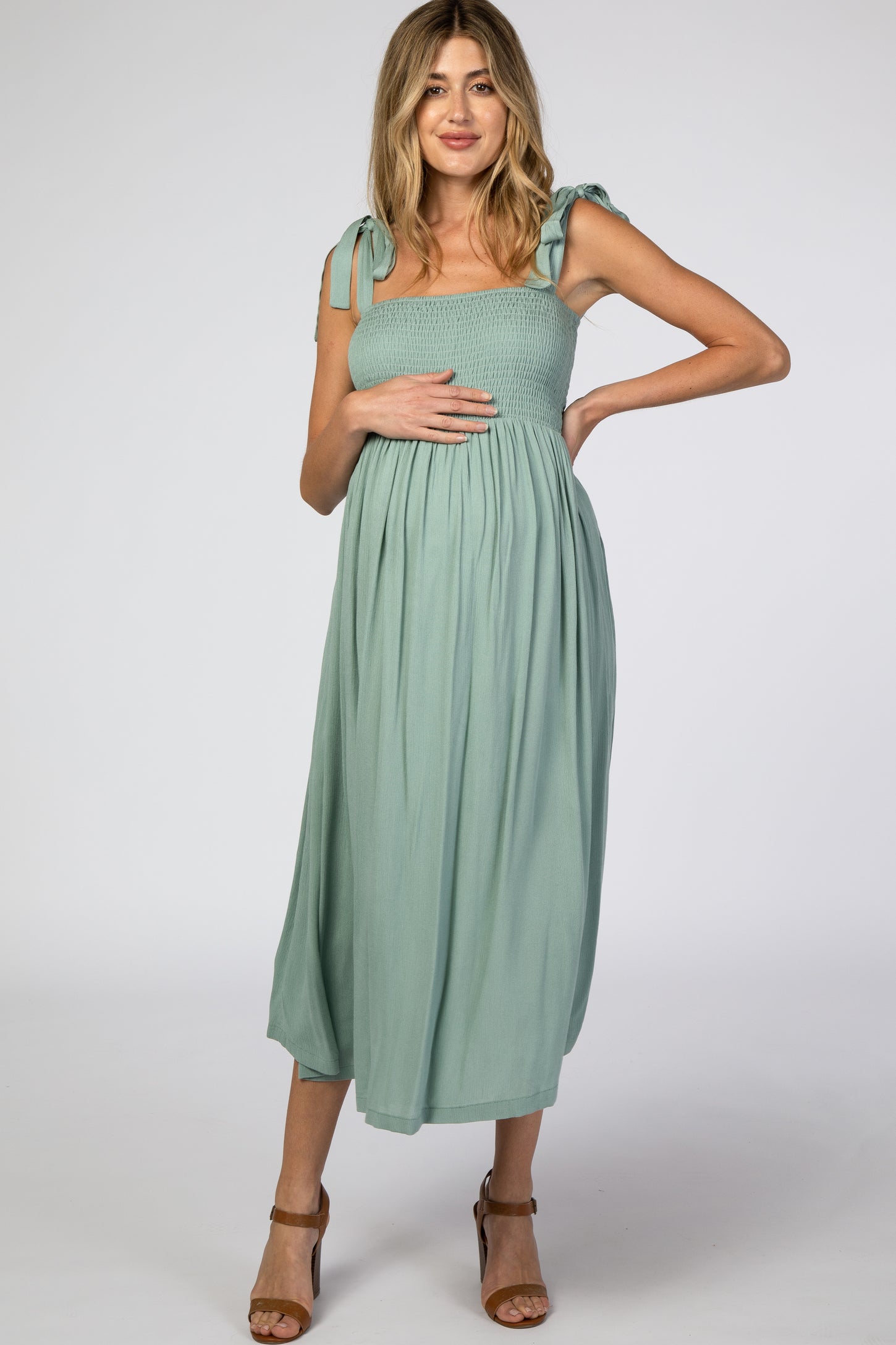 pregnant woman in a sage green smocked maternity midi dress with tie straps and brown heels