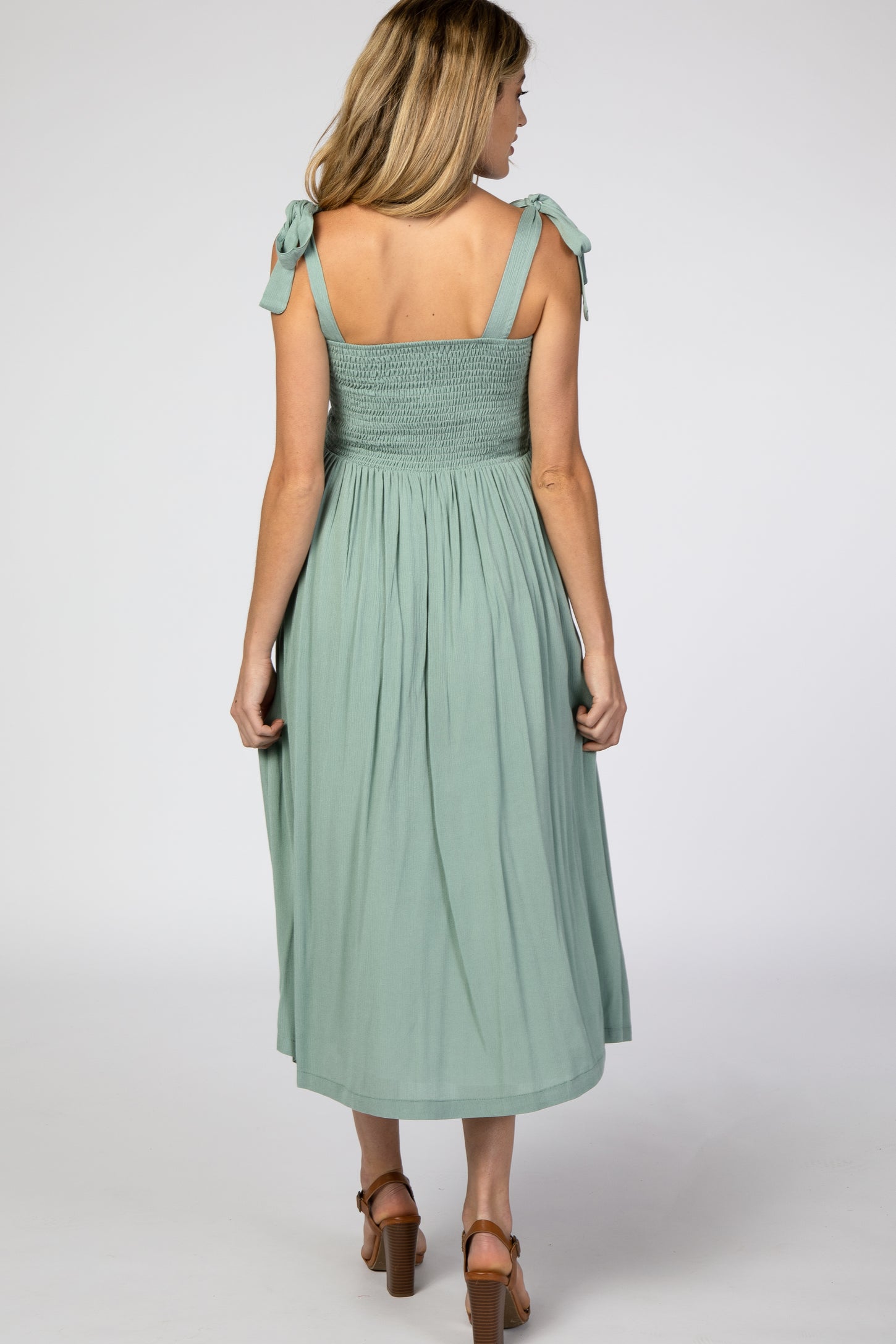 woman wearing a mint green maternity sundress with tie shoulder straps and a smocked bodice, showing a flowing skirt