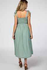 woman wearing a mint green maternity sundress with tie shoulder straps and a smocked bodice, showing a flowing skirt
