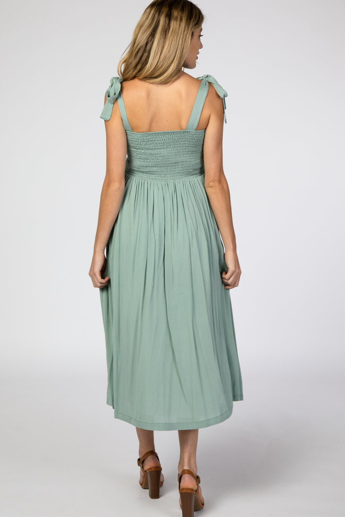 woman wearing a mint green maternity sundress with tie shoulder straps and a smocked bodice, showing a flowing skirt