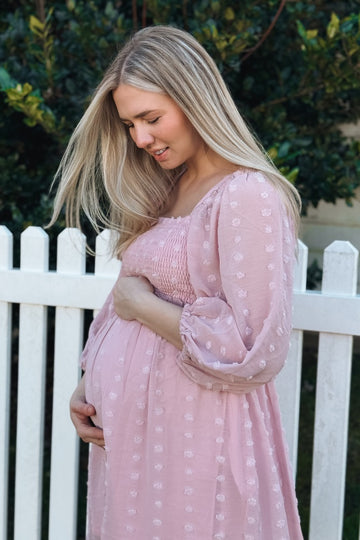 woman wearing a blush pink maternity dress with smocked bodice and puff sleeves, holding her baby bump