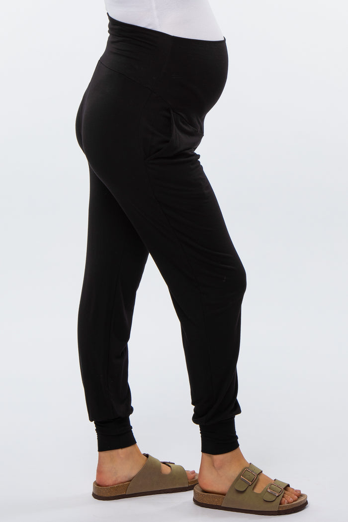 woman wearing black maternity joggers with a visible baby bump and brown sandals