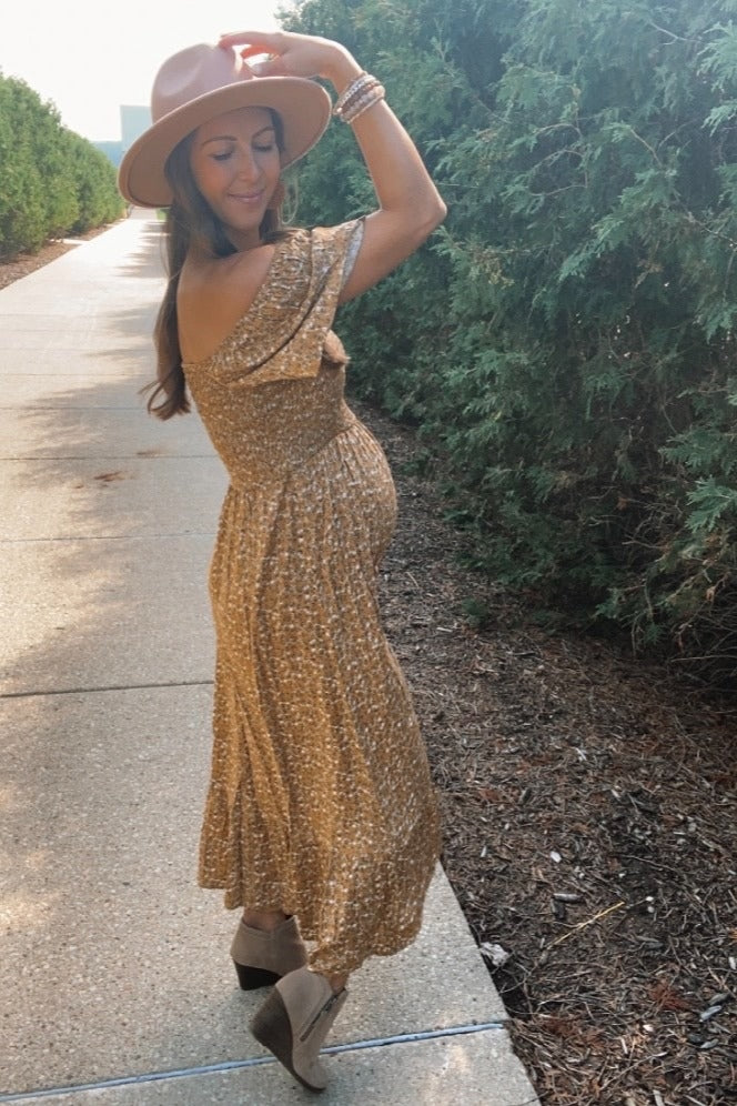 woman wearing a brown floral off-shoulder maternity dress and showing her baby bump while posing outdoors