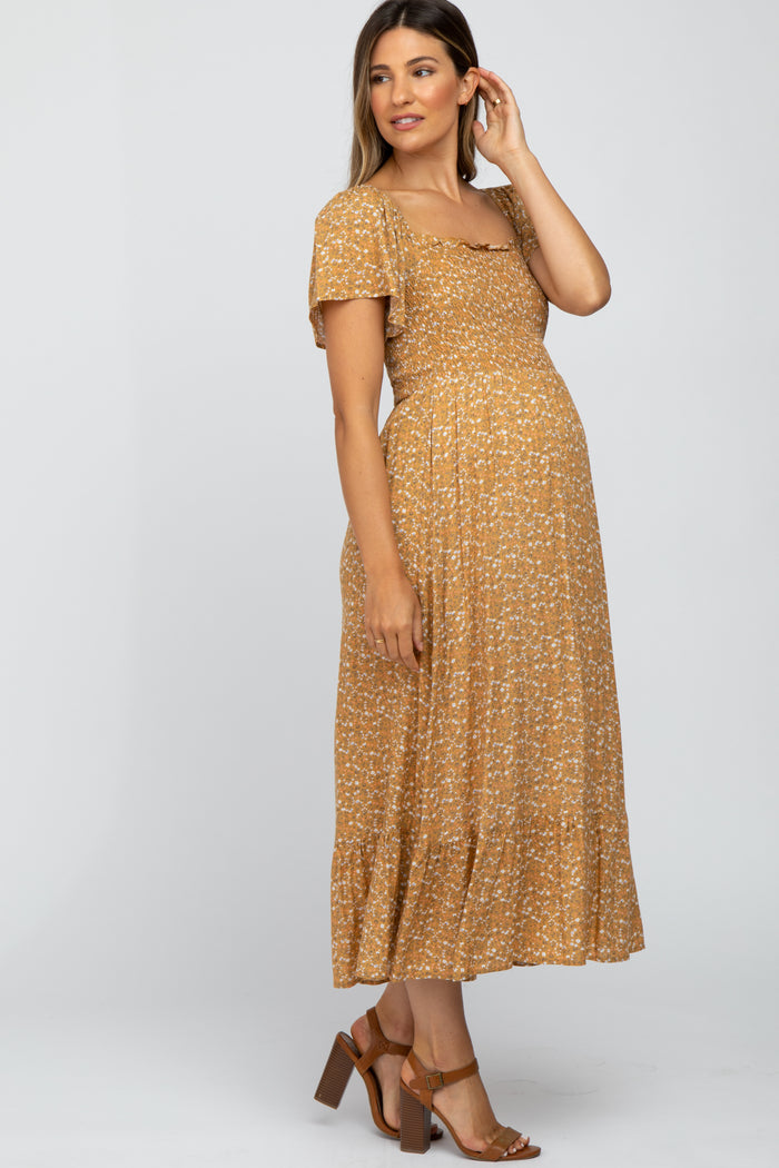 woman wearing a mustard brown floral maternity maxi dress with short sleeves and a fitted bodice, showing her baby bump