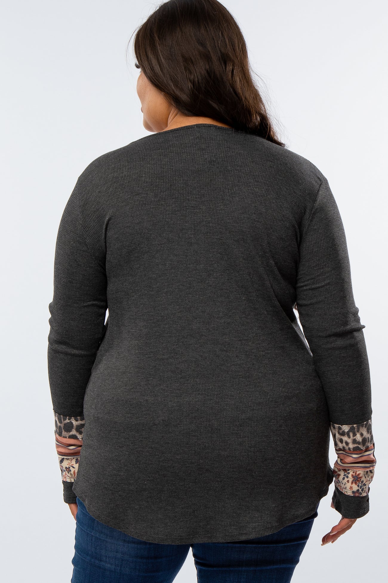 woman wearing a dark gray long sleeve plus size top with patterned cuffs, viewed from the back