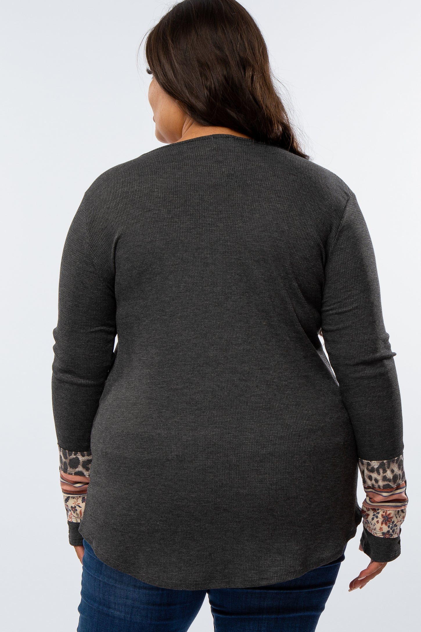 woman wearing a dark gray long sleeve plus size top with patterned cuffs, viewed from the back
