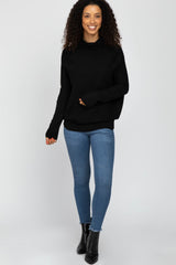 woman wearing a black oversized sweater with a cowl neck and blue skinny jeans