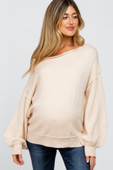 woman wearing a light beige oversized maternity sweater with wide sleeves and a visible baby bump