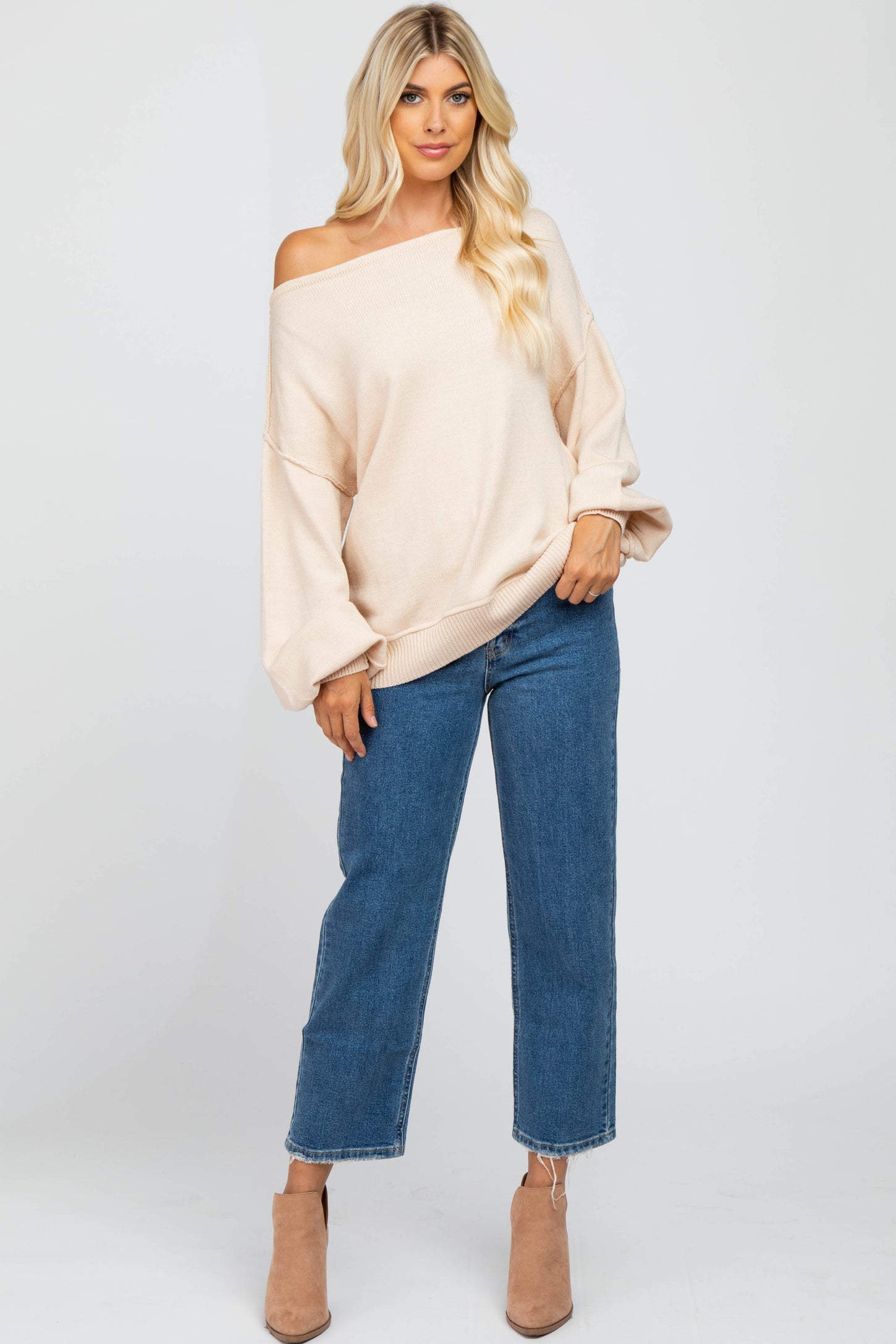 woman wearing a light beige off-shoulder sweater paired with high-waisted blue straight-leg jeans and taupe ankle boots