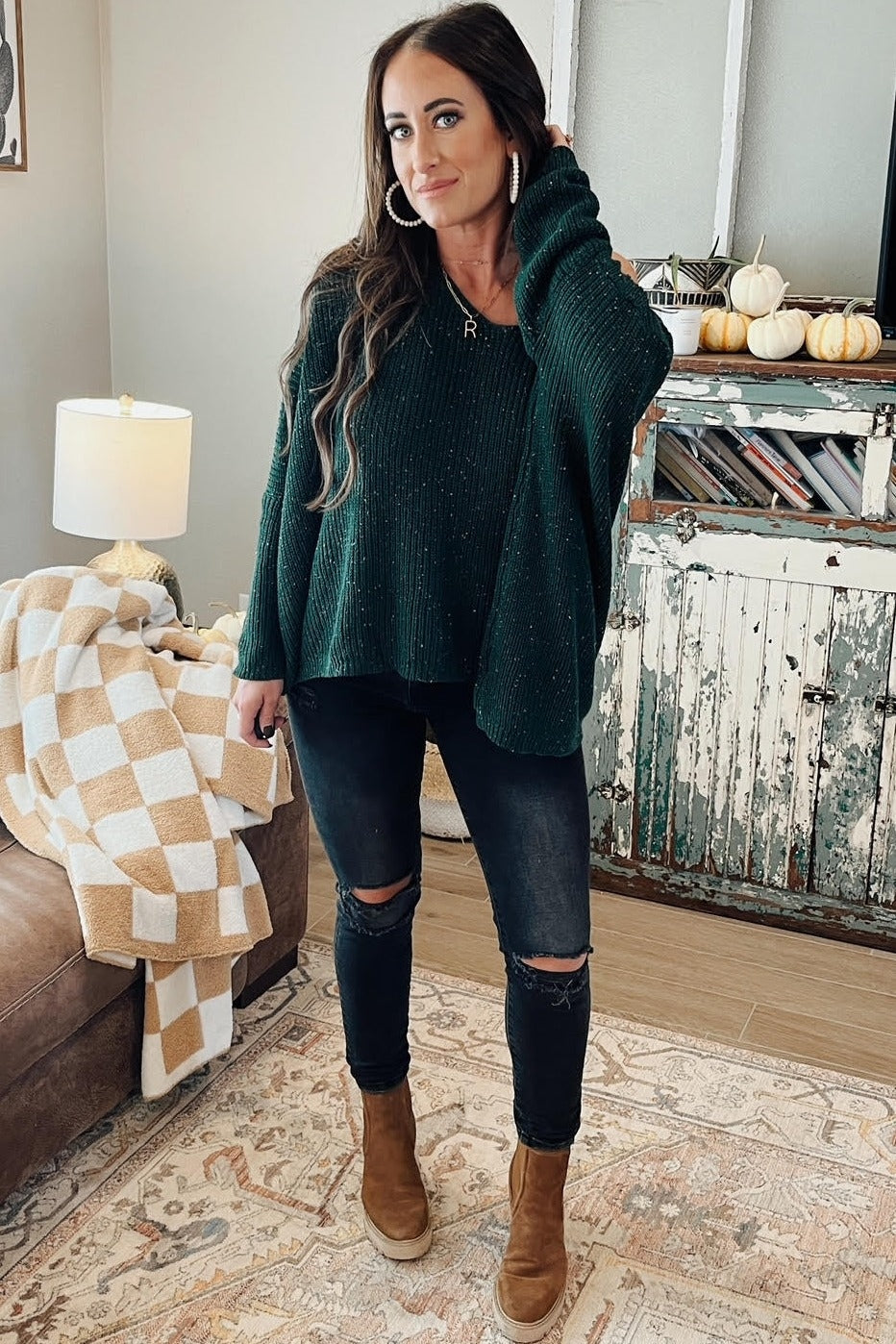 woman wearing a dark green oversized knitted sweater with a hood, black ripped skinny jeans, and brown ankle boots
