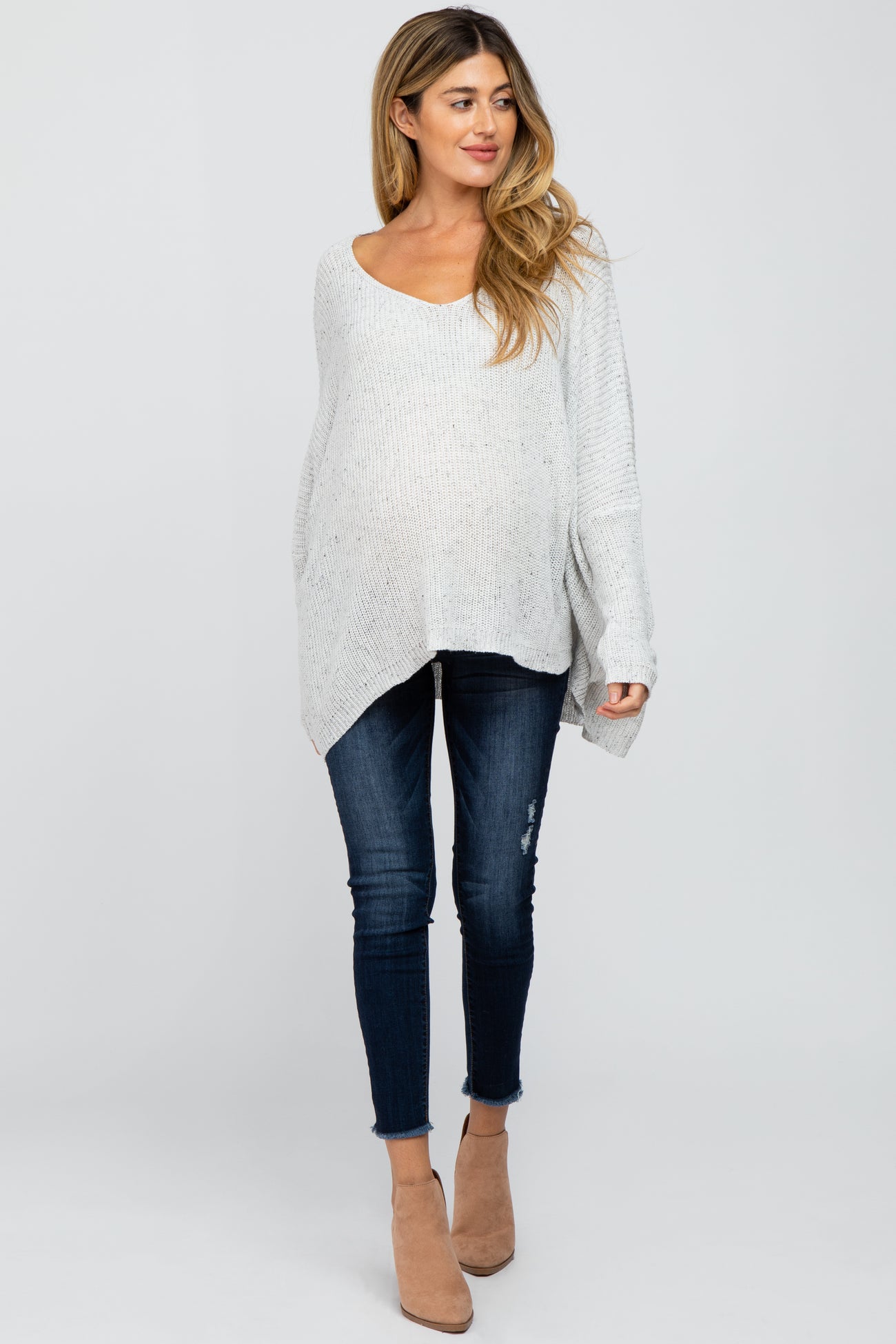 woman wearing a light gray oversized maternity sweater and dark blue distressed skinny jeans, showing her baby bump