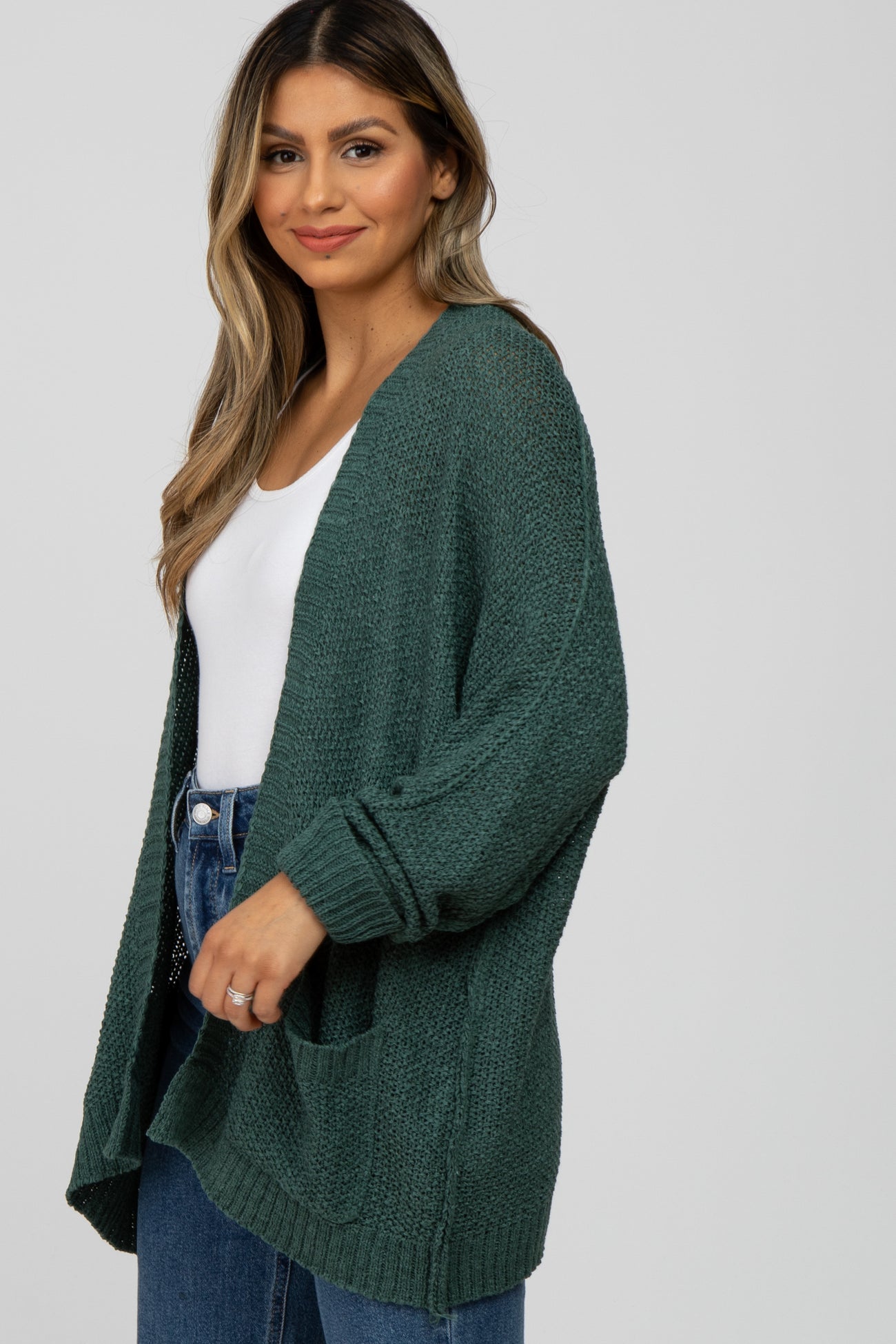 woman wearing a green oversized cardigan with pockets over a white top and blue jeans