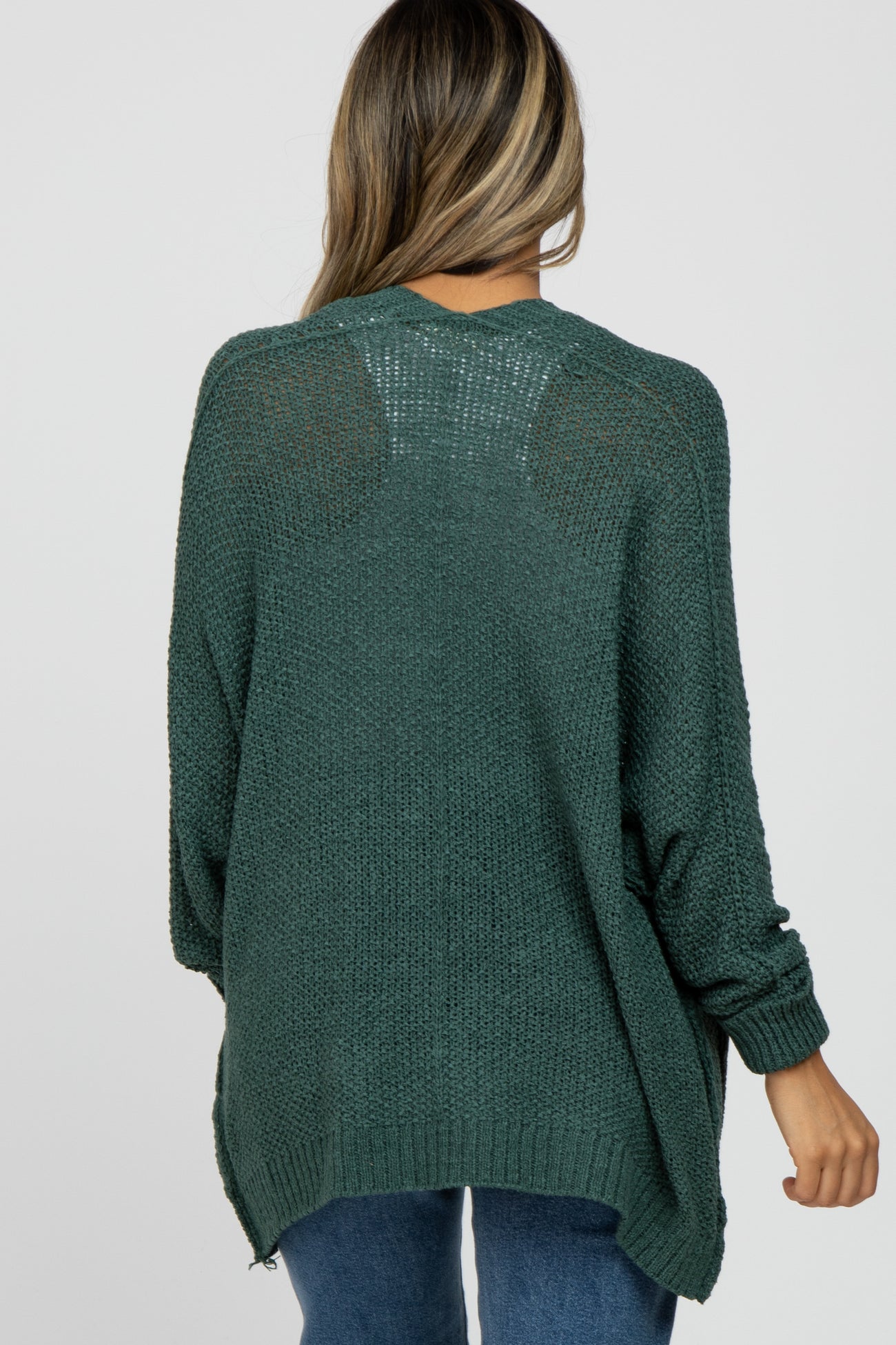 woman wearing a dark green oversized sweater with a textured knit design and side slits, seen from the back
