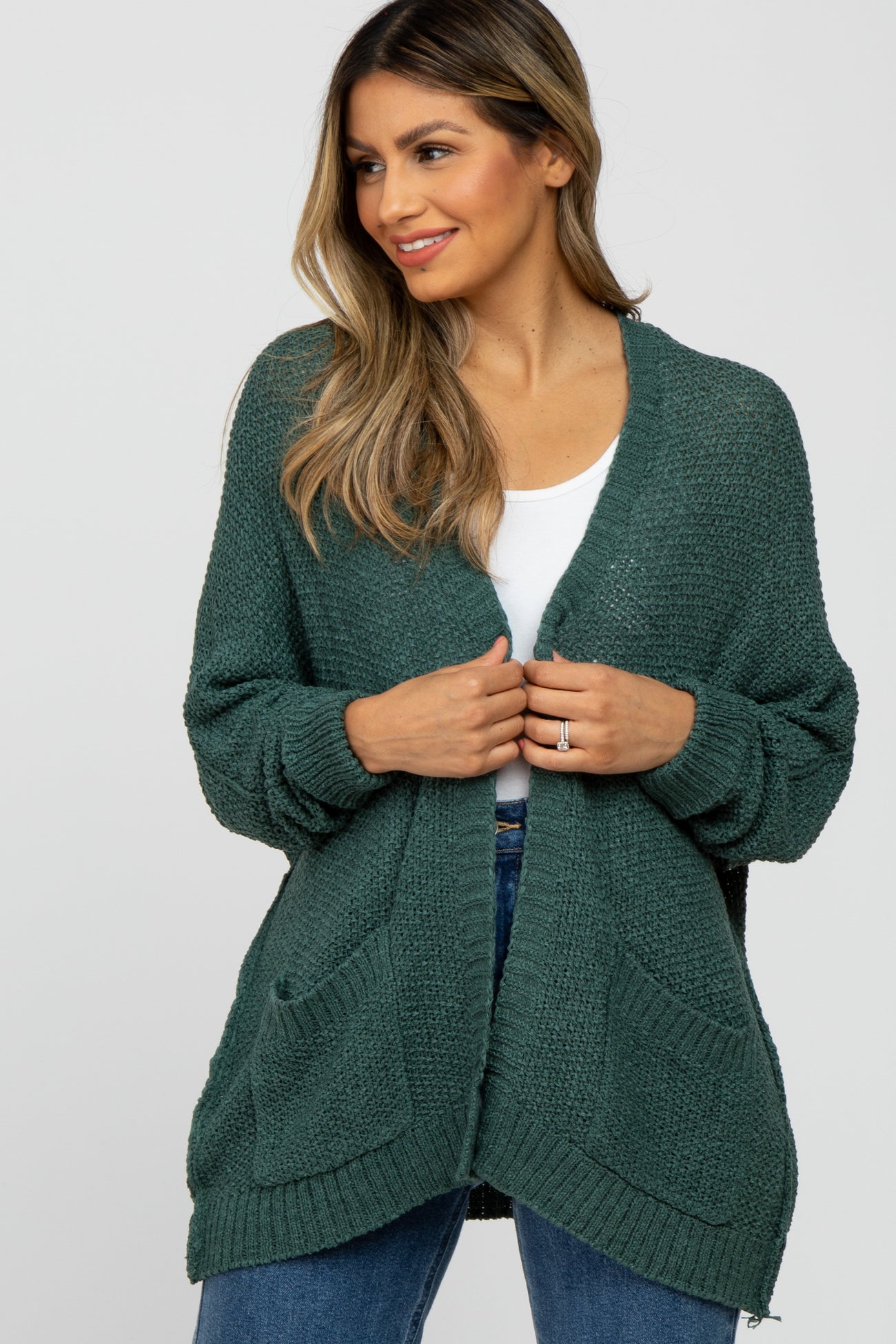 woman wearing a dark green open front knit cardigan with pockets over a white top and blue jeans