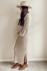 woman wearing a beige ribbed maternity dress with side slits, holding her baby bump and wearing a wide-brimmed hat