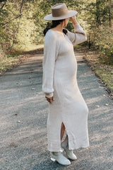 woman wearing a beige ribbed maternity dress with side slits and long sleeves, holding her hat, showcasing her baby bump