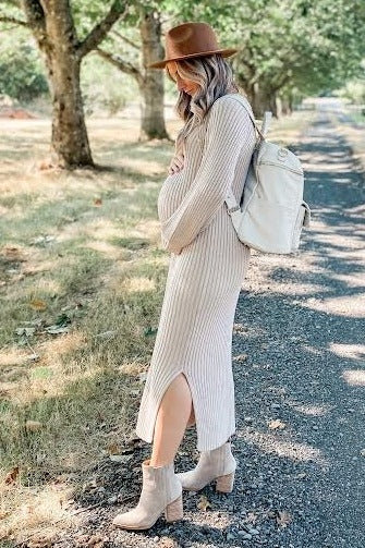 woman wearing a cream and beige striped maternity dress with a side slit, holding her baby bump and carrying a backpack