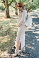 woman wearing a cream and beige striped maternity dress with a side slit, holding her baby bump and carrying a backpack