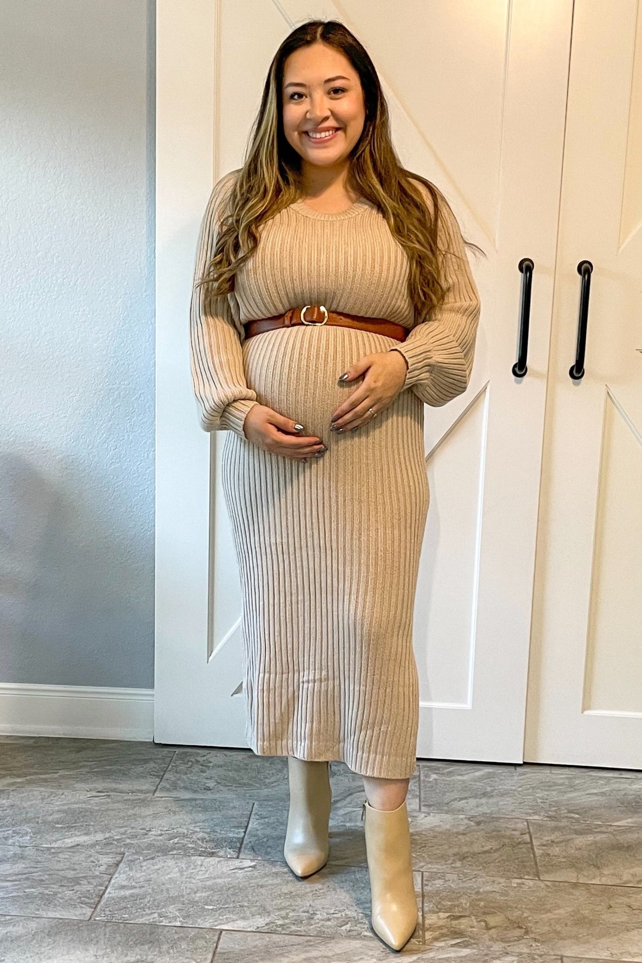 woman wearing a beige ribbed maternity dress with a brown belt and holding her baby bump