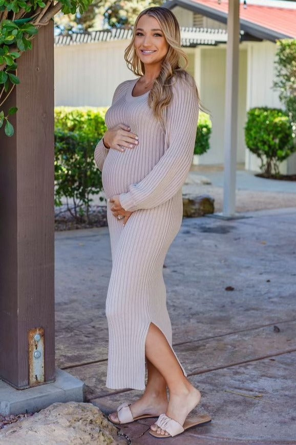 woman wearing a beige ribbed maternity dress with side slits and holding her baby bump