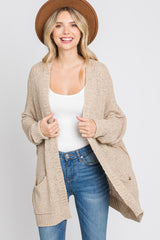 woman wearing a beige open knit cardigan with two front pockets and a white tank top, smiling and wearing a hat
