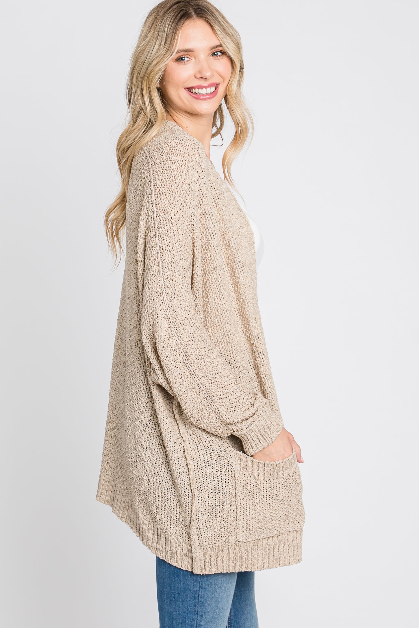 woman wearing a beige open-knit cardigan with a relaxed fit and side pockets, styled over a white top and blue jeans
