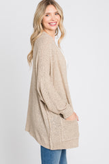 woman wearing a beige open-knit cardigan with a relaxed fit and side pockets, styled over a white top and blue jeans