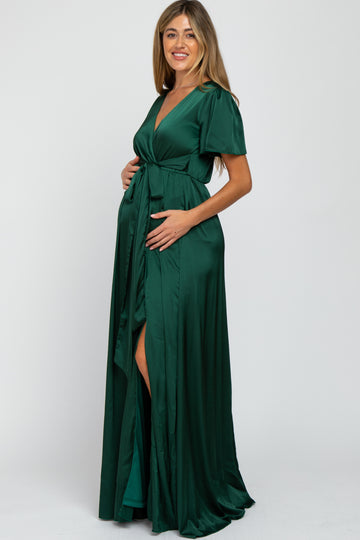 woman wearing a dark green maternity gown with short sleeves and a high slit, holding her baby bump