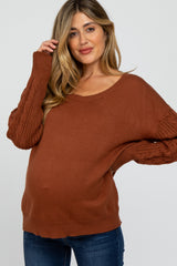 woman wearing a rust-colored maternity sweater with knitted sleeves and a visible baby bump